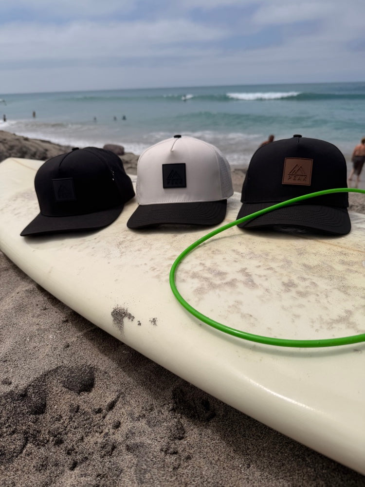 Three PEAK hats on surfboard at beach